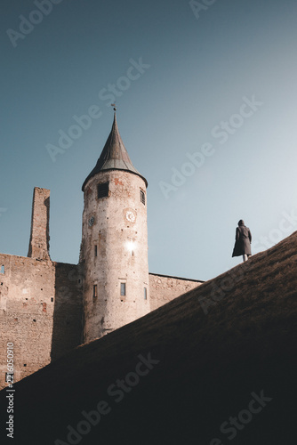View of Haapsalu Castle with its stone tower and a person standing on the grassy rampart under a clear blue sky in Haapsalu, Laane County, Estonia.