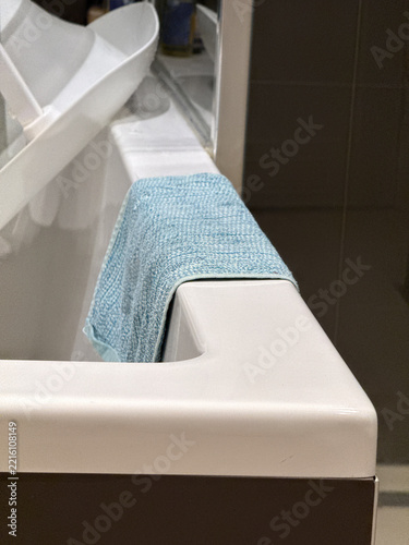 A pale blue towel hangs over the white edge of a modern bathtub beside a curved shower screen and tiled bathroom wall.