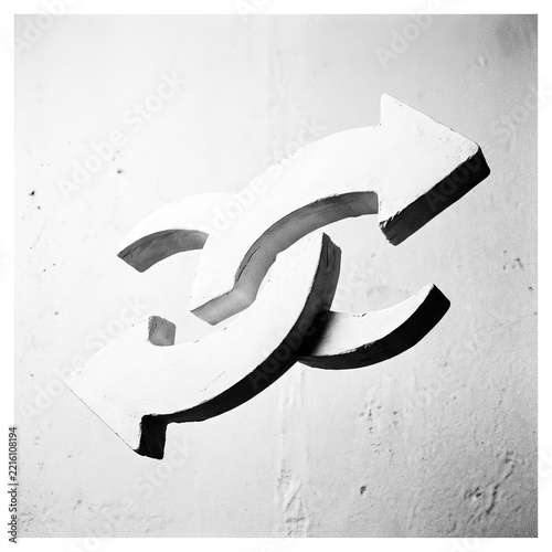 Minimalist black and white conceptual art featuring two interlocking white arrows on a textured wall symbolizing connection and flow.