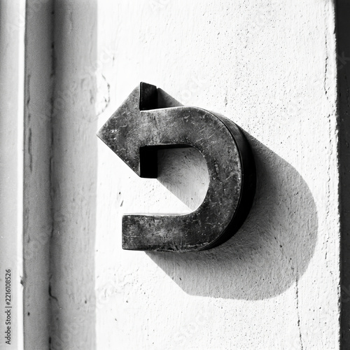 Artistic black and white shot of a metallic U-turn arrow mounted on a wall with deep shadows and industrial texture.