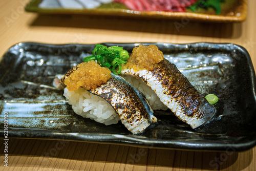 Closeup of Aburi Iwashi nigiri sushi, which is flame-seared Japanese sardine sushi served over seasoned sushi rice with grated daikon and spring onions. 