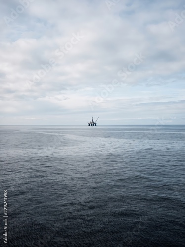 Offshore oil platform on open sea beneath cloudy sky. Marine petroleum drilling and energy production. Offshore industry and fossil fuel infrastructure. Minimal seascape with copy space.