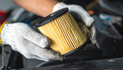 Car Oil Filter Replacement: A pair of gloved hands holds a used oil filter, symbolizing car maintenance and the need for regular vehicle servicing.