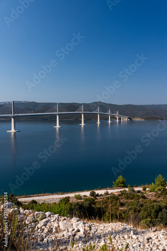 Panoramic view of Peljesac Bridge spanning deep blue bay from hillside, Croatia