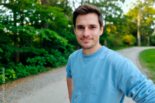 Portrait of Caucasian young adult man standing on park path and looking at camera, conveying active lifestyle and wellbeing. Useful for fitness, wellness, outdoor health campaigns