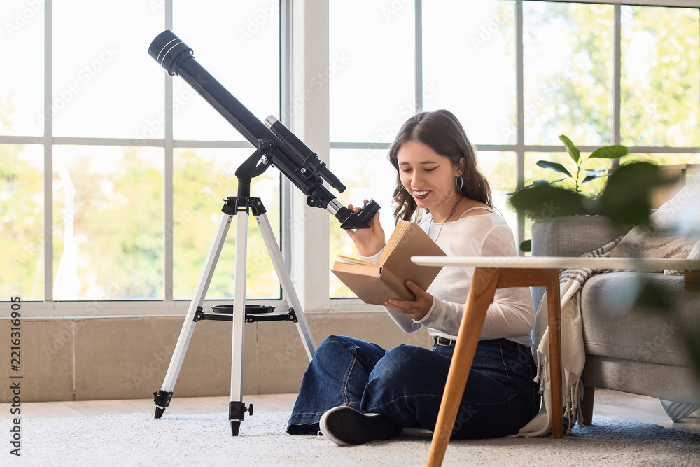 Fototapeta premium Astronomy hobby and lifelong learning, young woman reading a book while using a telescope at home for science education and personal development