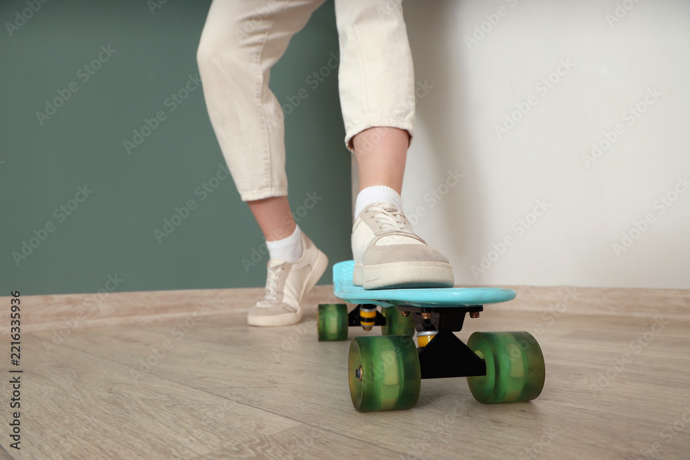 Naklejka premium Urban lifestyle and youth culture, person standing on a blue plastic skateboard wearing casual sneakers and trousers in a modern home interior