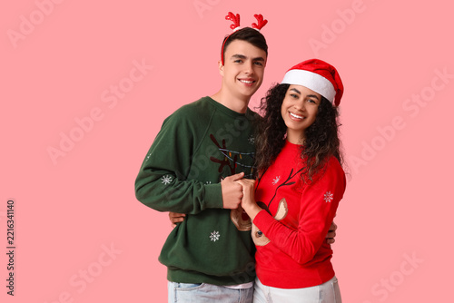 Happy young couple in Christmas sweaters on pink background