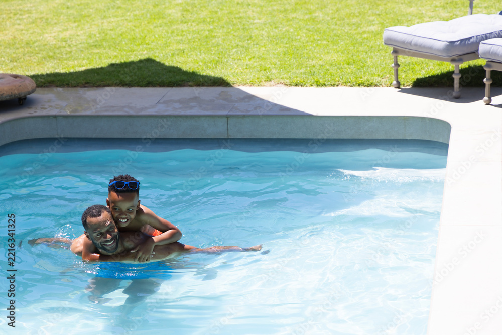 Naklejka premium African American family playing in backyard pool, father carrying child with blue goggles