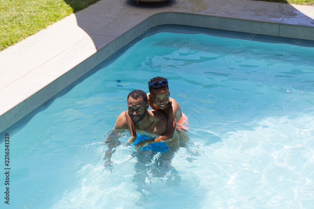 Naklejka premium African American father and son playing in backyard pool holding blue pool toy and goggles
