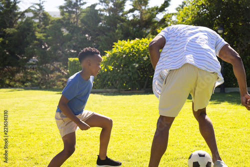 African American mature and youth males playing soccer on lawn, with ball, youth in sneakers