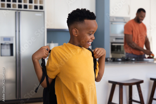 African American dad and child in kitchen dad cooking child adjusting black backpack, copy space