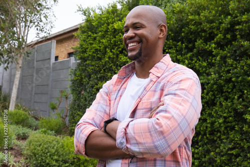 African American man posing arms crossed looking right in yard in plaid shirt, smartwatch
