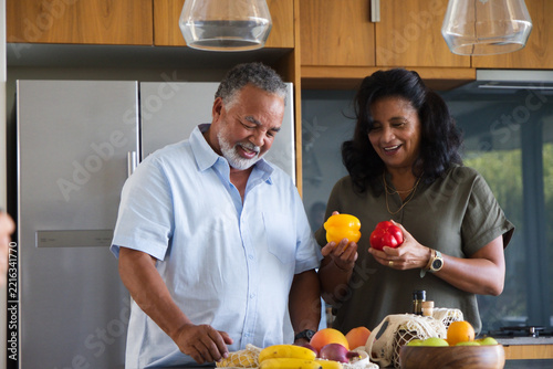 Senior couple standing at kitchen counter sorting fresh produce with mesh bags and peppers