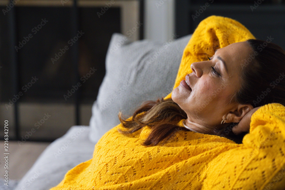 Fototapeta premium African American woman reclining on grey sofa in living room wearing bright yellow knit sweater
