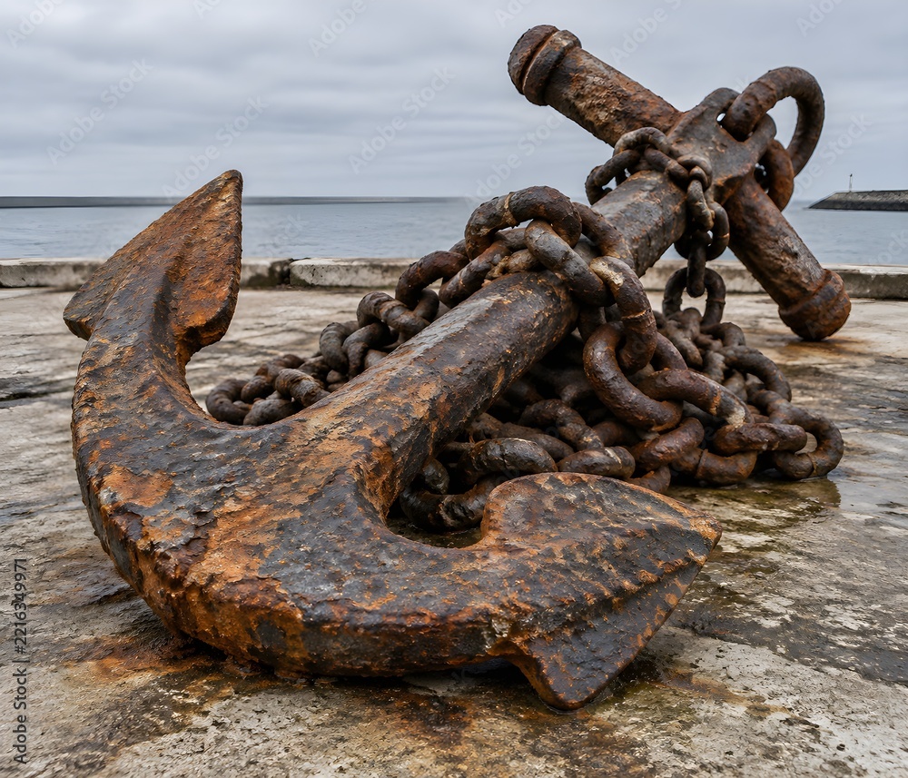 Fototapeta premium Large ship anchor lying on a stone quay with heavy iron chain