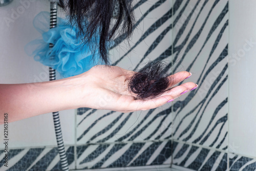 Woman hand with fallen black hair and split hair ends in domestic bathroom