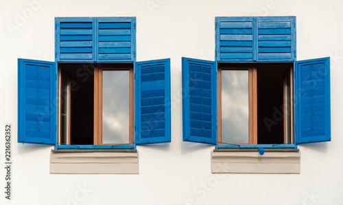 Two brown windows with blue shutters on a white wall