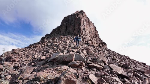 Extreme hiker carefully scrambling up a dangerous, steep, and rocky mountain summit. The adventurous person is climbing toward the peak