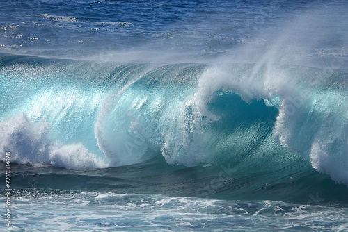 Powerful rolling turquoise ocean wave with white sea spray blowing off the top
