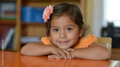 A young girl with a flower in her hair smiles sweetly at the camera