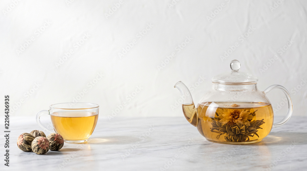 Glass teapot with blooming flower tea, cup and dried tea balls on ...