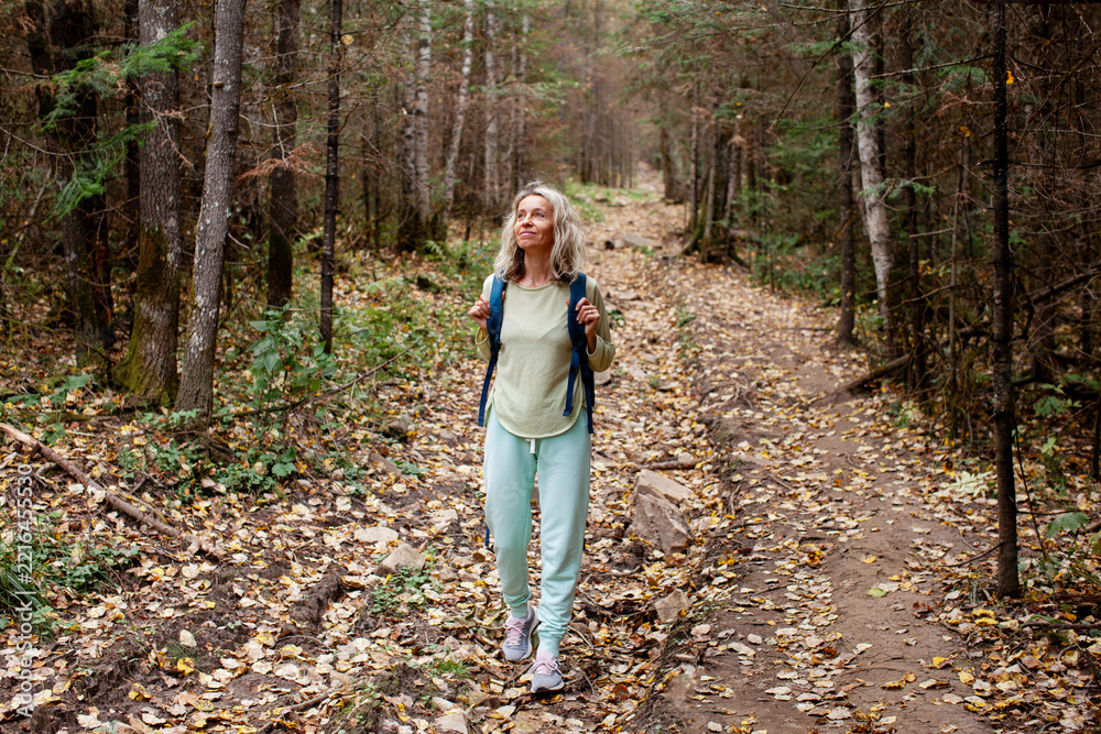 Fototapeta premium Middle aged woman hiking a forest trail during a digital detox. Nature walk and mindful outdoor break. Screen free lifestyle, personal wellbeing and unplugged living.