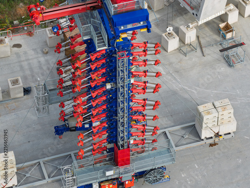 Aerial view of a specialized launching gantry machine used for high speed rail construction featuring red hydraulic arms and a blue steel frame on a concrete site in the United Kingdom.