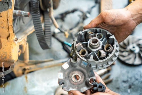 Mechanic holding a motorcycle CVT variator pulley with roller weights during transmission repair in a workshop.