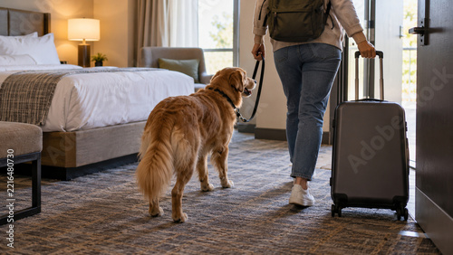 Traveler leaving pet-friendly hotel room with dog and suitcase