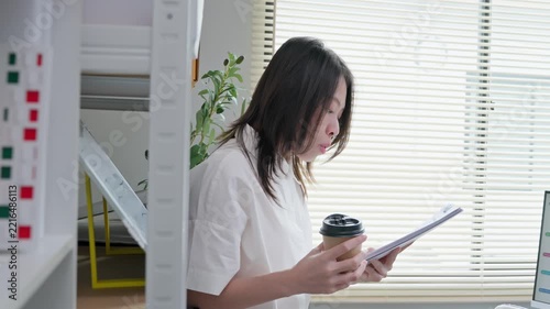 Asian Businesswoman Reading Documents and Holding Coffee Cup in Office
