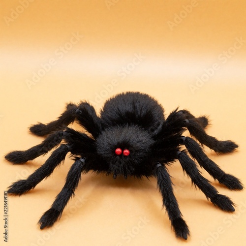 Black furry toy spider with red eyes on orange background