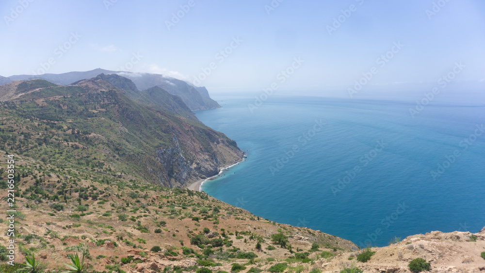 Fototapeta premium Panoramic view of mountainous coastal cliffs meeting deep blue sea with outdoors
