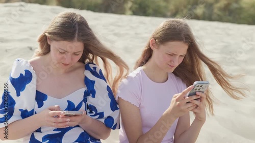 A woman and girl are sitting on the beach with phones slow motion medium shot