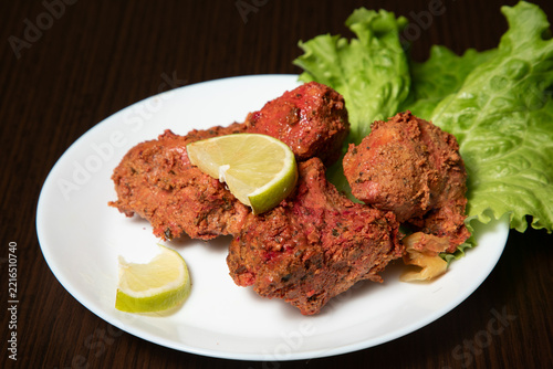 Groupe de morceaux de poulet tandoori sur une assiette blanche avec des tranches de citron