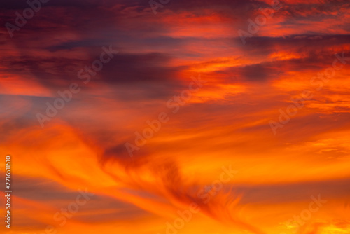 Fotografie Vibrant sky filled with fiery red and orange cloud wisps glowing in the dusk lig
