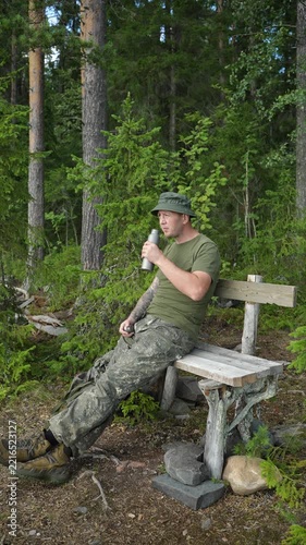 Hiker drinking water from a bottle on a wooden bench in a forest
