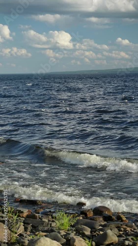 Waves rolling onto a stony lake shore with seagulls and cloudy blue sky