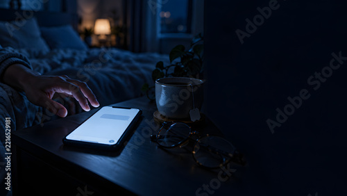 Hand Reaching for a Glowing Smartphone on a Bedside Table at Night in a Dark Bedroom, Insomnia and Late Night Phone Use