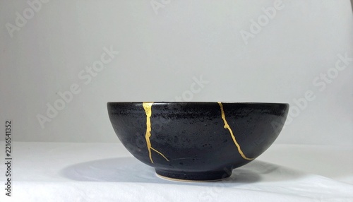 Kintsugi Repaired Black Ceramic Bowl with Gold Seams on White Background resilience concept