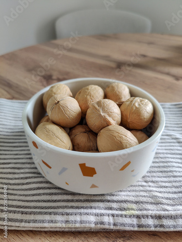 Whole walnuts in white ceramic bowl and striped kitchen cotton towel on wooden table.  Healthy eating, calories, diet, harvest. Shells of washed nuts are perfectly clean. Copy space. Close-up.