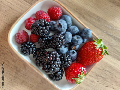 Small ceramic dish with mix of fresh berries: strawberries, blueberries, blackberries and raspberries. Healthy eating, natural vitamins. Top view. Copy space