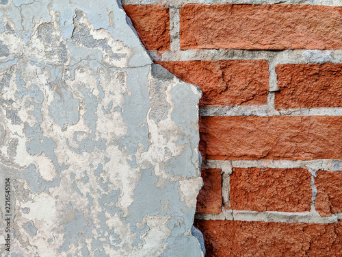 Сombination of rough red brick and smooth yet cracked gray plaster. Old brick wall with gray plaster that has crumbled away and traces of old paint. Copy space. Close-up