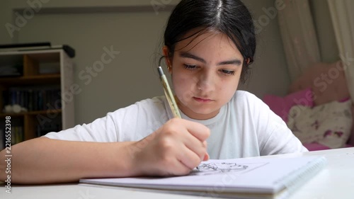 Young girl drawing and sketching on paper with a pencil at home, close-up focused shot.