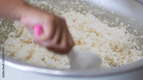 4K Chef hand holding white paddle to fluff cooked Jasmine rice inside large electric rice cooker pot, food preparation process for Asian cuisine.