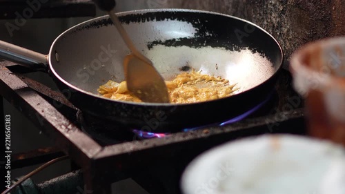 Chef using spatula to stir fry fresh squid rings with chili, garlic, and basil in a hot skillet over stove flame, showing cooking process for spicy Thai stir-fried squid concept.