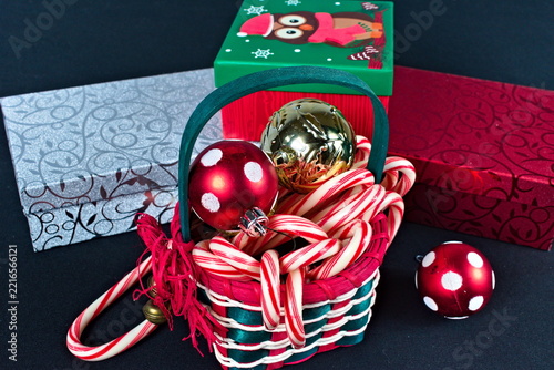 A small woven basket holds peppermint candy canes and decorative ornaments surrounded by colorful gift boxes featuring owl and floral patterns.