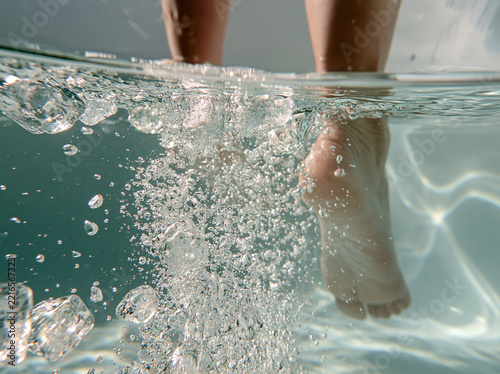 Underwater view of human legs and feet with bubbles in clear swimming pool water