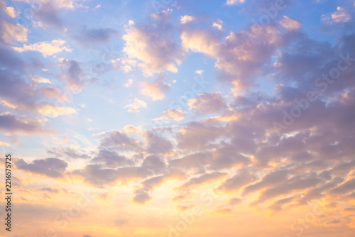 A beautiful scenic sunset sky filled with soft golden and pink colored fluffy cumulus clouds. Panoramic evening atmosphere nature landscape backdrop. Nature theme, sunset mood.