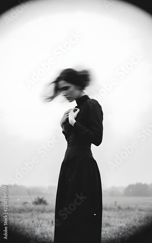 Monochromatic, surrealist portrait of a woman dressed in black outdoors.